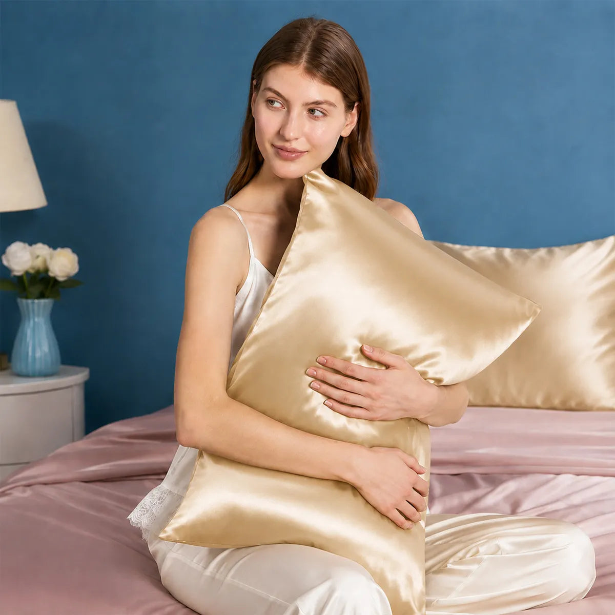 Model holding a champagne silk pillowcase in a bedroom
